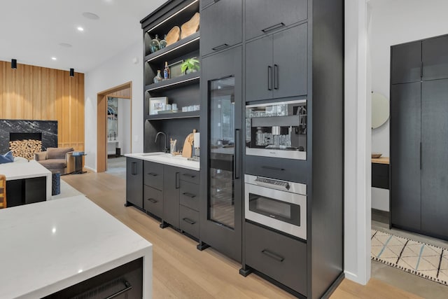 kitchen with light wood finished floors, a sink, open shelves, and stainless steel oven