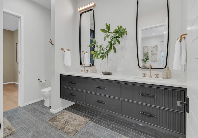 bathroom featuring a sink, baseboards, toilet, and double vanity