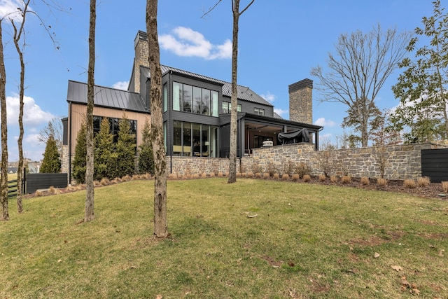 rear view of property with fence, a lawn, metal roof, a chimney, and a standing seam roof