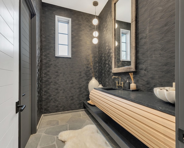 bathroom featuring double vanity, wallpapered walls, stone finish flooring, and a sink