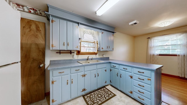 kitchen with light floors, a peninsula, blue cabinetry, freestanding refrigerator, and a sink