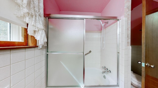 bathroom featuring tile walls, toilet, and shower / bath combination with glass door