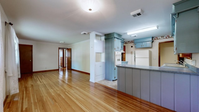 kitchen featuring white appliances, baseboards, a peninsula, a sink, and light wood-type flooring