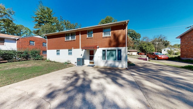 rear view of house with concrete driveway, a yard, brick siding, and central AC