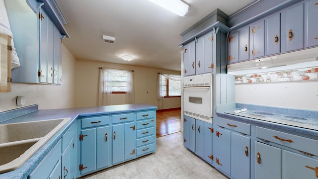 kitchen with white oven, blue cabinets, a peninsula, and a sink