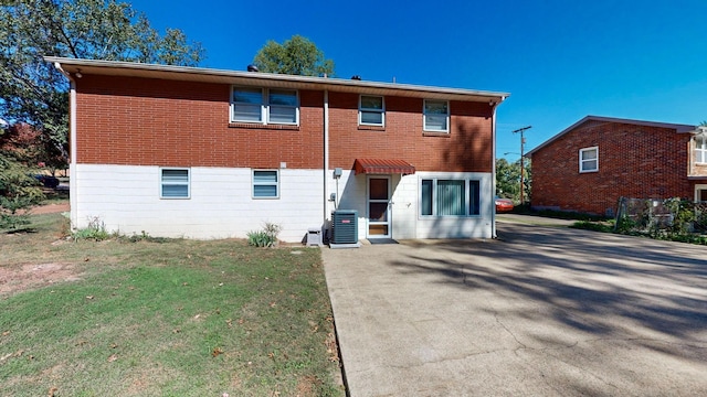 rear view of property with brick siding, a lawn, driveway, and central AC