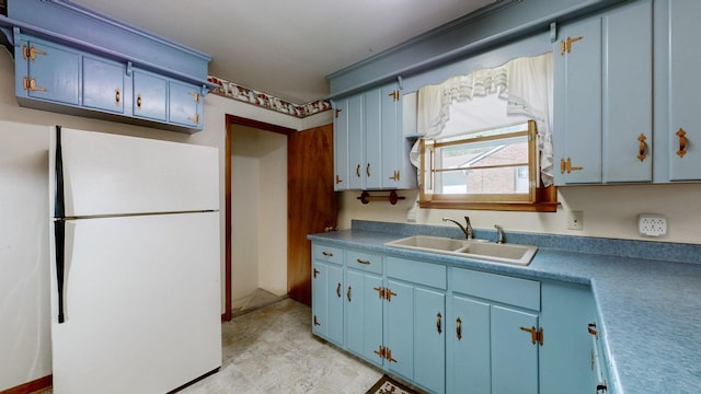 kitchen featuring blue cabinetry, freestanding refrigerator, and a sink