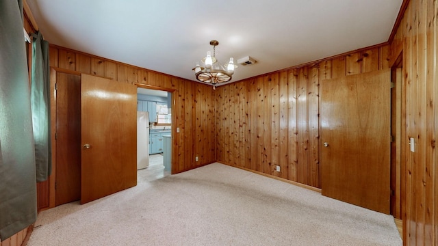 interior space with light carpet, a notable chandelier, ornamental molding, freestanding refrigerator, and wooden walls