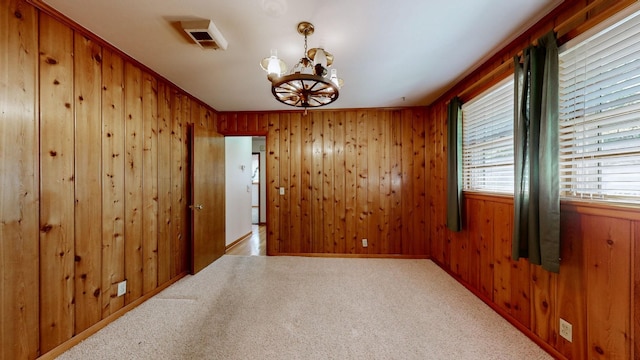 unfurnished room featuring a notable chandelier, carpet, and wood walls