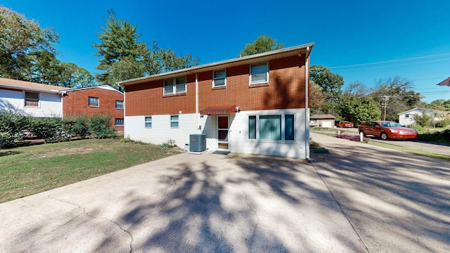 rear view of house featuring cooling unit, a lawn, and brick siding