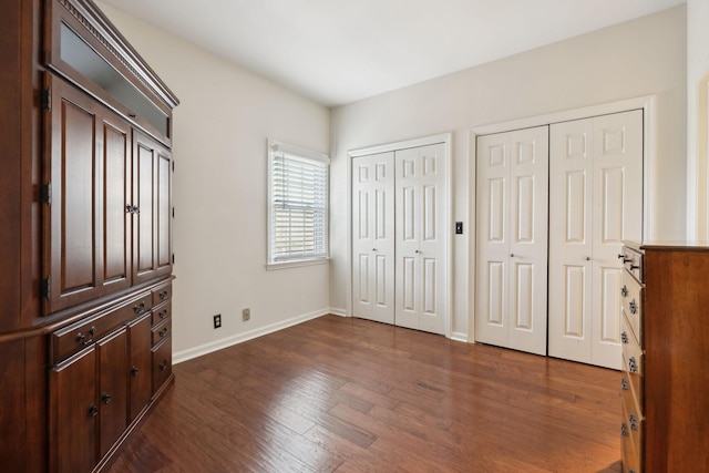 bedroom featuring dark wood-style floors, two closets, and baseboards