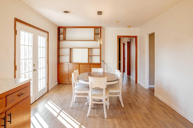 dining space featuring french doors, baseboards, light wood-style flooring, and crown molding