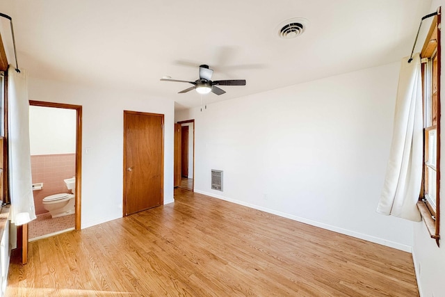 unfurnished bedroom with tile walls, light wood-style floors, visible vents, and connected bathroom