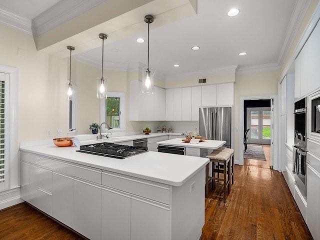 kitchen with crown molding, a peninsula, white cabinets, stainless steel appliances, and dark wood-style flooring