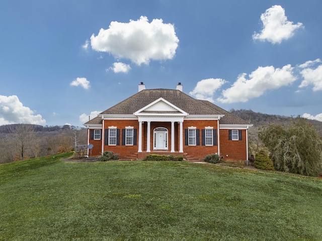 neoclassical home featuring brick siding, a chimney, and a front yard