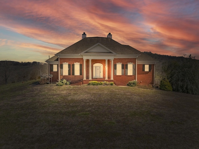 neoclassical / greek revival house featuring a front yard, brick siding, and a chimney