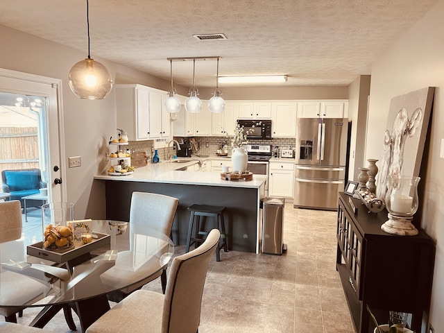 kitchen with a sink, tasteful backsplash, appliances with stainless steel finishes, a peninsula, and white cabinets