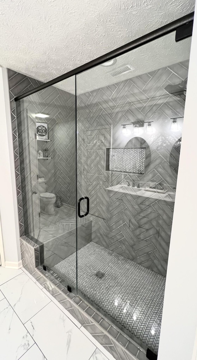 bathroom with toilet, marble finish floor, a shower stall, and a textured ceiling