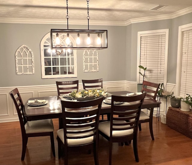 dining space with visible vents, ornamental molding, dark wood-type flooring, wainscoting, and a decorative wall