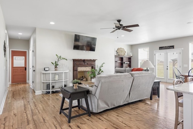 living room with a ceiling fan, baseboards, recessed lighting, a fireplace with raised hearth, and light wood-style floors