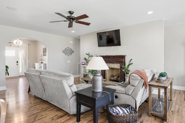 living room featuring baseboards, ceiling fan, hardwood / wood-style floors, a fireplace, and arched walkways