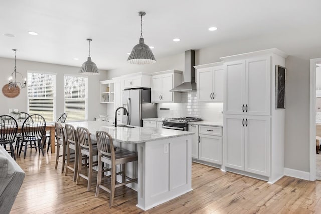 kitchen featuring a center island with sink, stainless steel appliances, white cabinets, a kitchen bar, and wall chimney range hood