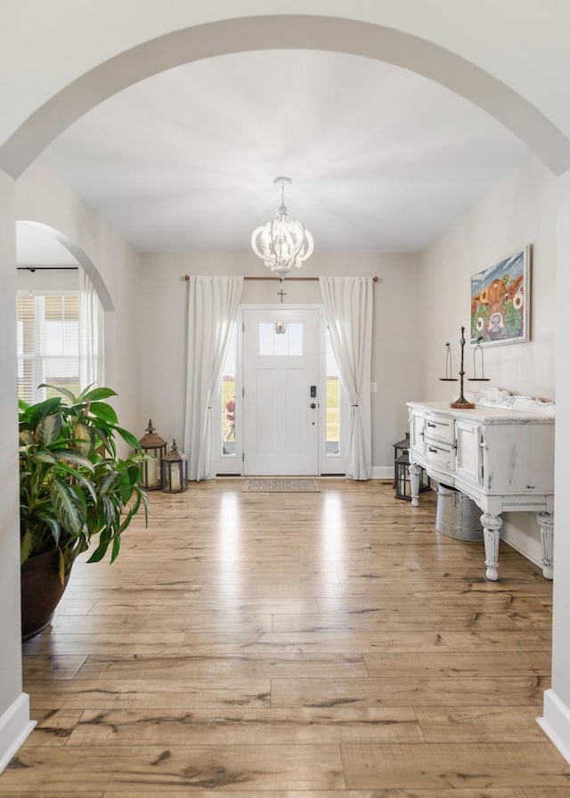 entryway with plenty of natural light, an inviting chandelier, baseboards, and light wood-style floors