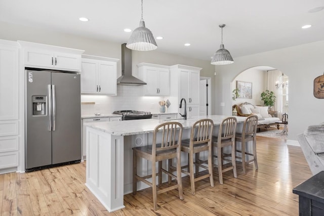 kitchen featuring white cabinetry, wall chimney exhaust hood, arched walkways, and stainless steel appliances