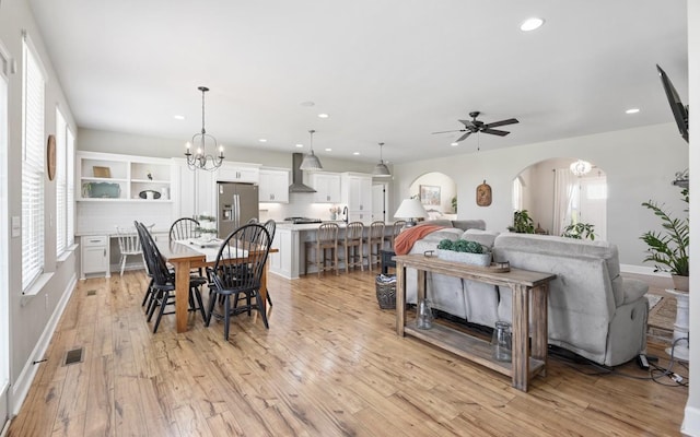 dining area with a wealth of natural light, ceiling fan with notable chandelier, arched walkways, and light wood finished floors