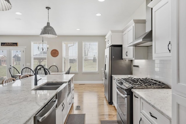 kitchen featuring backsplash, wall chimney range hood, appliances with stainless steel finishes, light wood-style floors, and white cabinets