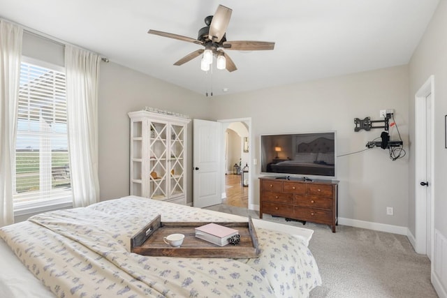 bedroom with baseboards, arched walkways, light colored carpet, and a ceiling fan