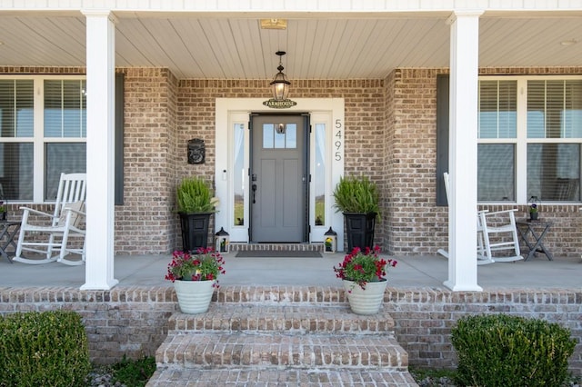 doorway to property with a porch and brick siding