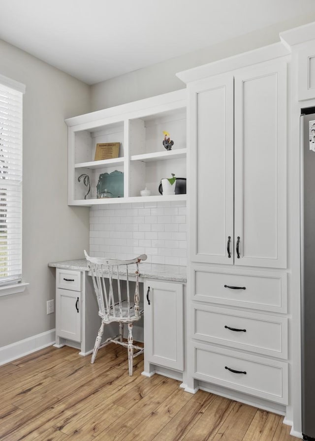 office area featuring baseboards, light wood finished floors, and built in study area