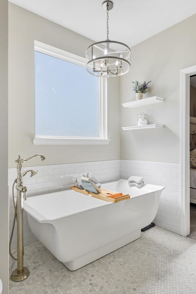 ensuite bathroom with a wainscoted wall, a freestanding bath, ensuite bathroom, an inviting chandelier, and tile walls