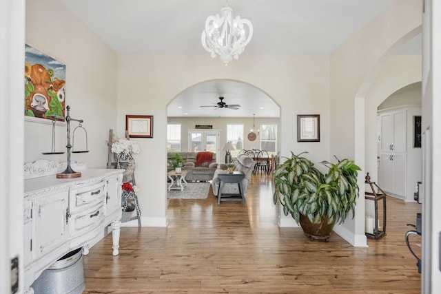 entryway with baseboards, light wood-style flooring, recessed lighting, arched walkways, and ceiling fan with notable chandelier