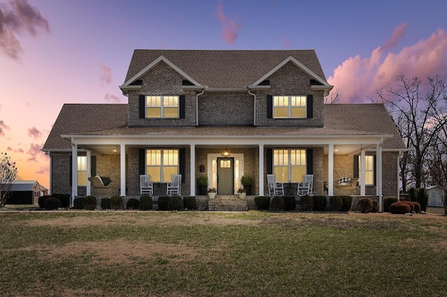 craftsman house with brick siding, covered porch, a front lawn, and a shingled roof