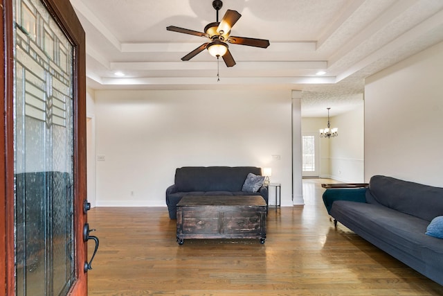 living area with ceiling fan with notable chandelier, baseboards, a tray ceiling, and wood finished floors