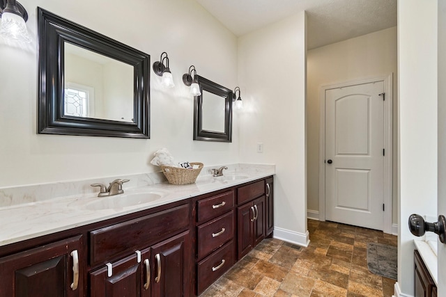 bathroom featuring double vanity, stone finish flooring, baseboards, and a sink