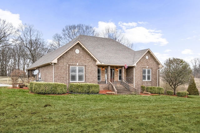 view of front of house featuring brick siding, a shingled roof, a front yard, and fence