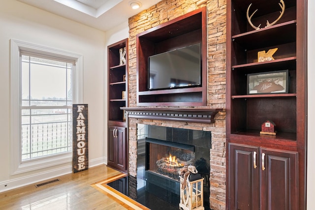 living room featuring built in features, wood finished floors, visible vents, baseboards, and a stone fireplace