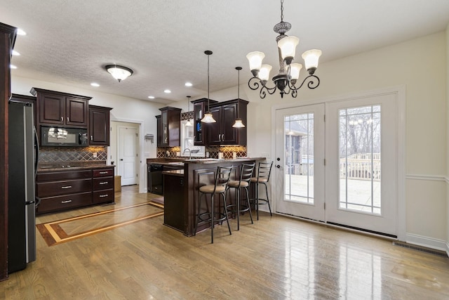 kitchen with dark brown cabinets, a peninsula, light wood-style floors, and black microwave