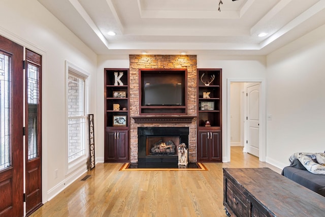 living room with a tray ceiling, built in shelves, and light wood-style flooring