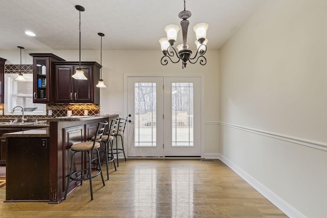 kitchen with dark countertops, light wood finished floors, dark brown cabinetry, a breakfast bar, and decorative backsplash