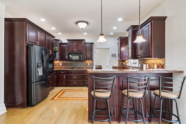 kitchen with a peninsula, hanging light fixtures, black appliances, light wood-style floors, and tasteful backsplash