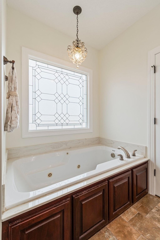 bathroom featuring a chandelier, stone finish flooring, and a whirlpool tub