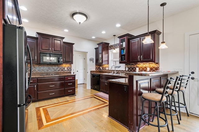 kitchen featuring glass insert cabinets, a peninsula, hanging light fixtures, black appliances, and a sink
