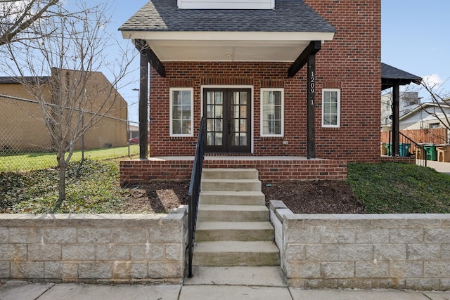 view of front of property featuring brick siding, french doors, roof with shingles, and fence