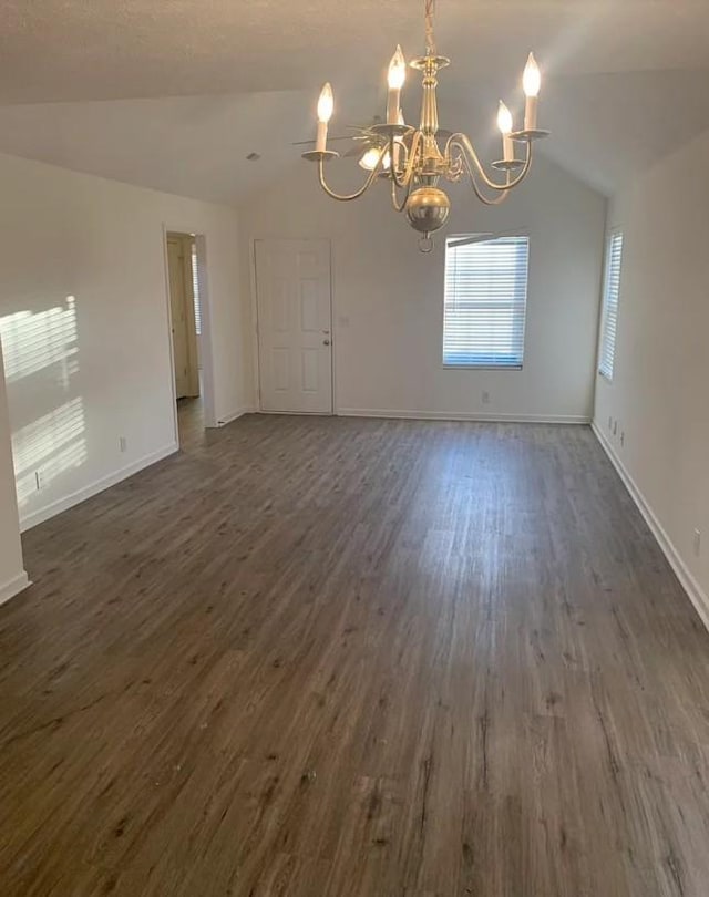 spare room featuring an inviting chandelier, vaulted ceiling, baseboards, and dark wood-type flooring