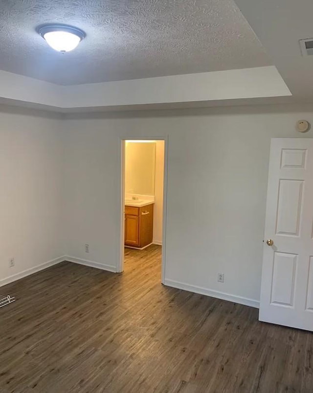 empty room featuring dark wood-style floors, visible vents, a textured ceiling, and baseboards