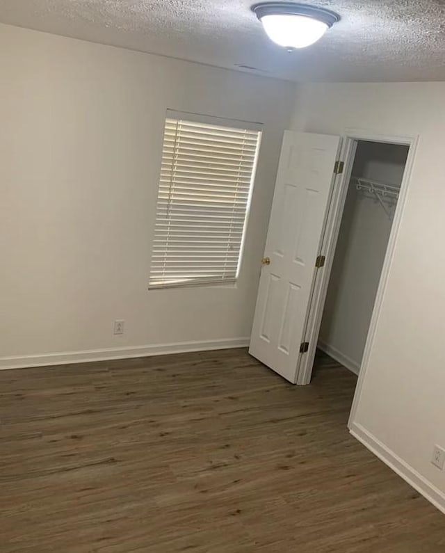 unfurnished bedroom featuring a textured ceiling, dark wood-style floors, a closet, baseboards, and a spacious closet